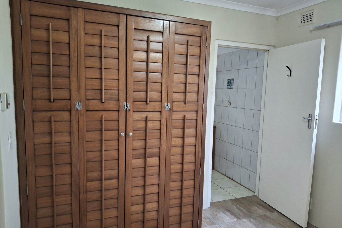 A bedroom featuring built-in wooden louvered wardrobes, tiled flooring, and direct access to an adjoining tiled bathroom area.