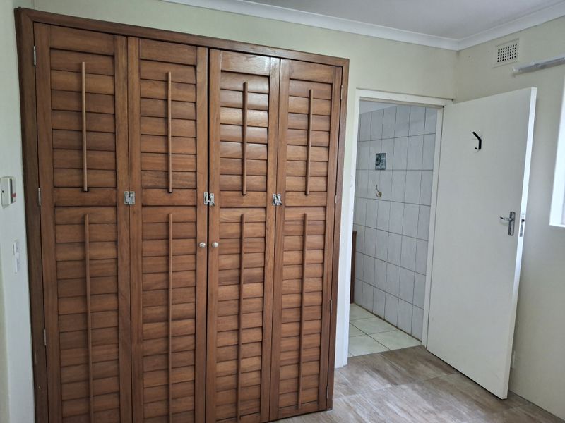 A bedroom featuring built-in wooden louvered wardrobes, tiled flooring, and direct access to an adjoining tiled bathroom area.