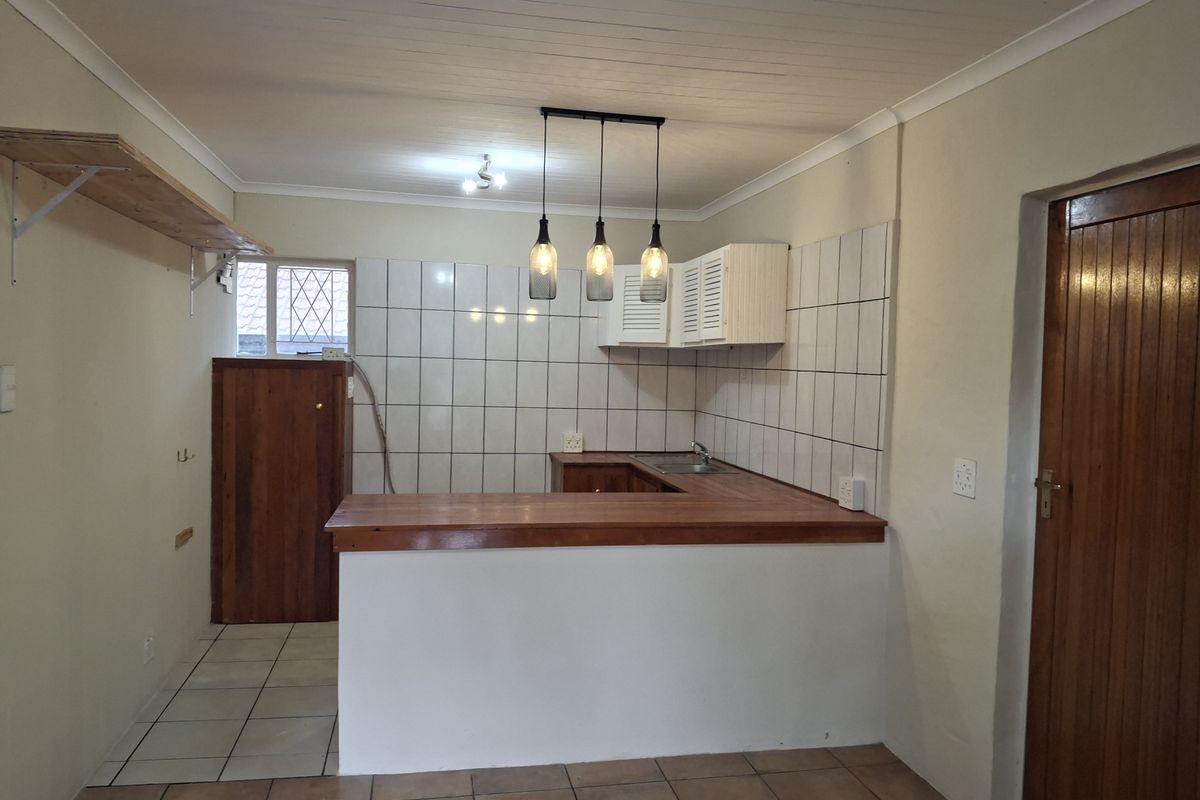 A functional kitchen area featuring a wooden breakfast bar, tiled splashback, built-in cabinetry, and a stainless steel sink, with a neutral color palette.