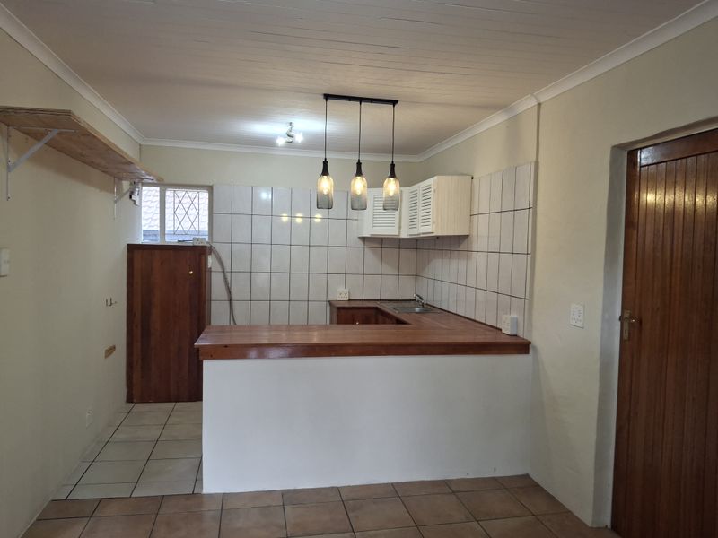 A functional kitchen area featuring a wooden breakfast bar, tiled splashback, built-in cabinetry, and a stainless steel sink, with a neutral color palette.