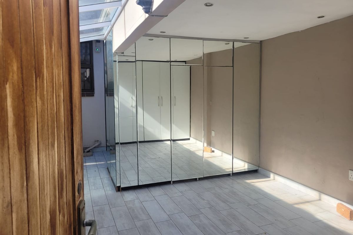 A bright, empty bedroom featuring extensive built-in mirrored wardrobes, tiled flooring, and a unique glass roof section providing natural light.
