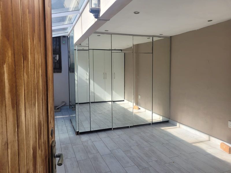 A bright, empty bedroom featuring extensive built-in mirrored wardrobes, tiled flooring, and a unique glass roof section providing natural light.