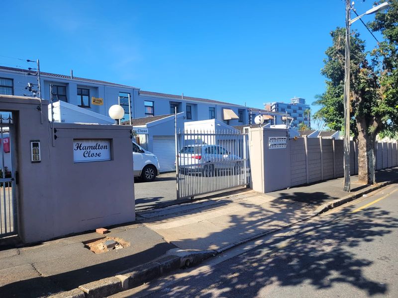 Front entrance view of Hamilton Close townhouse complex featuring a secure gated access point, perimeter walling, and electric fencing.