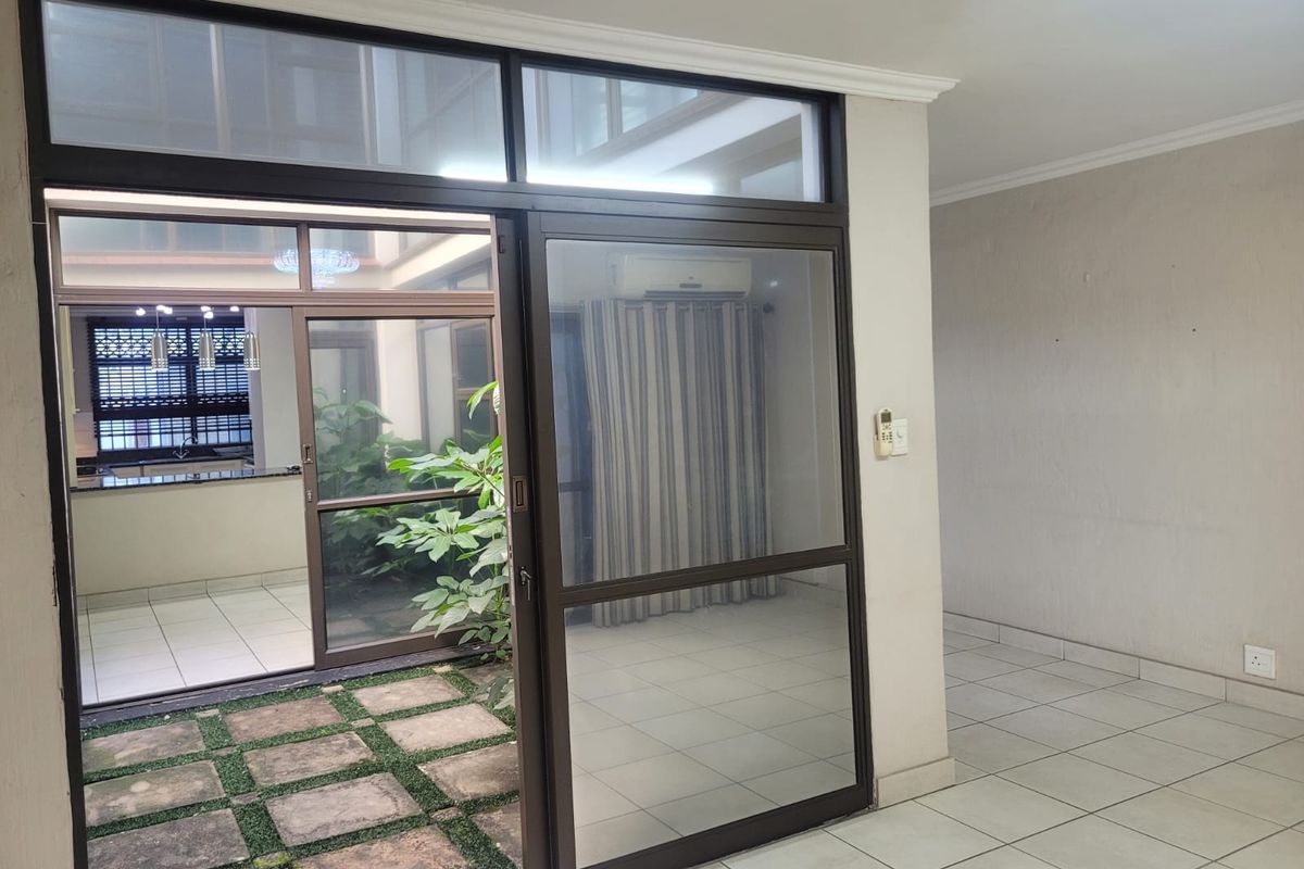 An empty living area featuring tiled floors and a large sliding glass door opening onto a central internal courtyard with paved stones.
