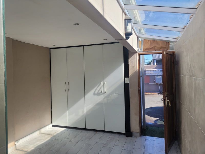 An entrance area featuring built-in cupboards, tiled flooring, and a glass roof panel providing natural light through a timber door.