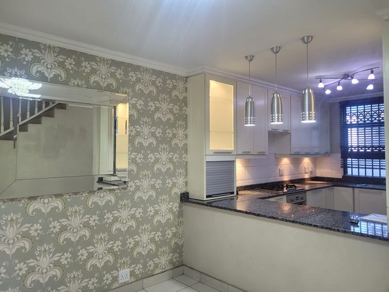 A well-lit kitchen featuring granite countertops, built-in cabinetry, integrated appliances, and decorative wallpaper, offering a functional and clean culinary space.