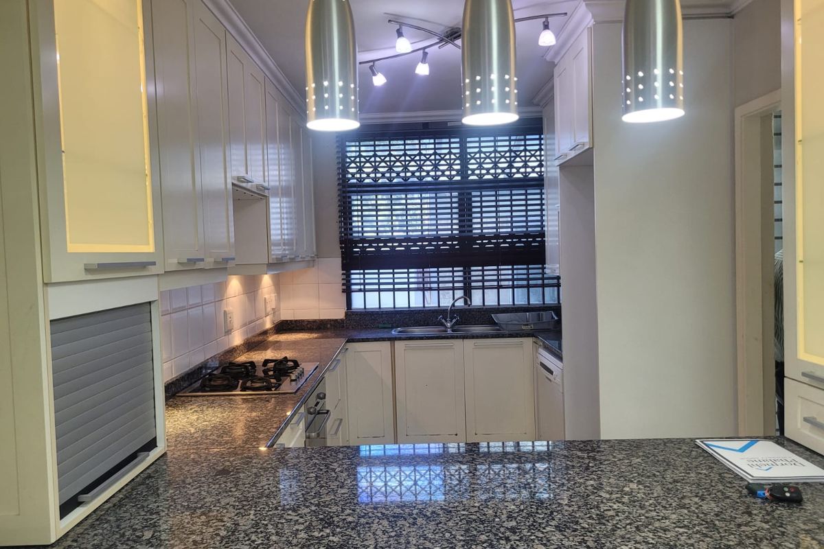 A well-maintained kitchen featuring granite countertops, a gas hob, built-in cabinetry, and modern pendant lighting, offering a functional and clean workspace.
