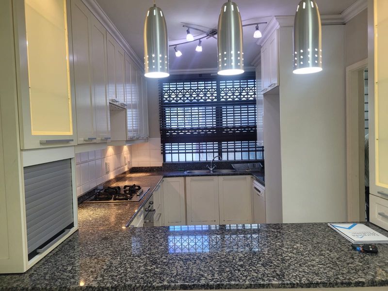 A well-maintained kitchen featuring granite countertops, a gas hob, built-in cabinetry, and modern pendant lighting, offering a functional and clean workspace.