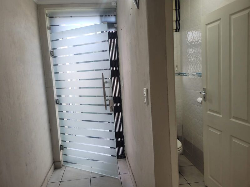 A hallway area featuring a modern frosted glass door and access to a small bathroom with tiled flooring.