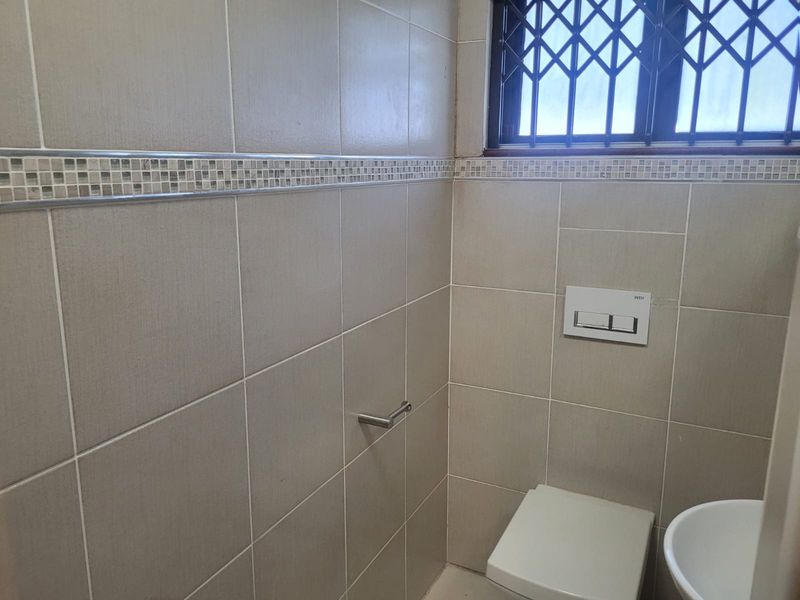 A clean, modern bathroom featuring neutral wall tiles with a decorative mosaic border and a wall-mounted toilet system.