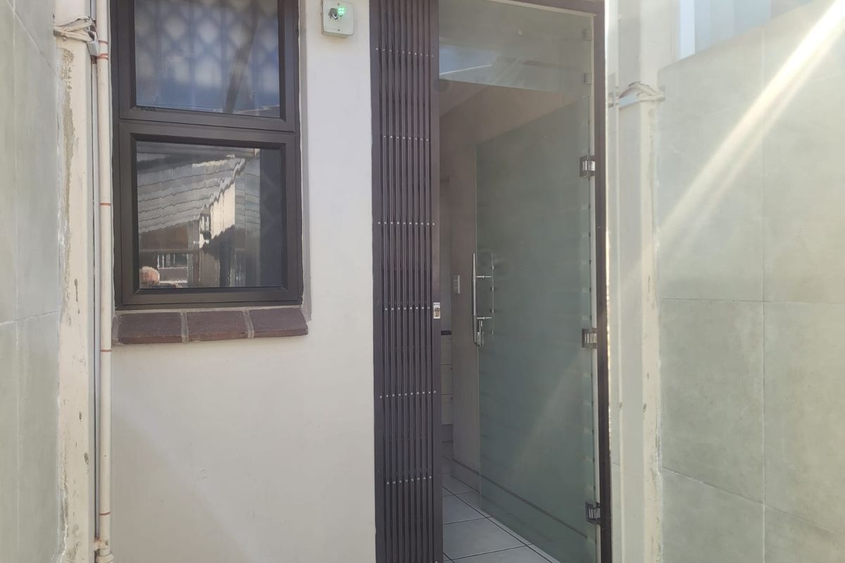 Exterior view of a rear entrance featuring a security gate and a frosted glass door leading into the tiled interior.