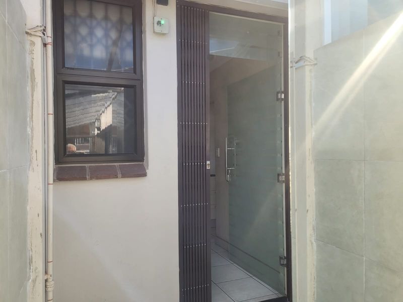 Exterior view of a rear entrance featuring a security gate and a frosted glass door leading into the tiled interior.