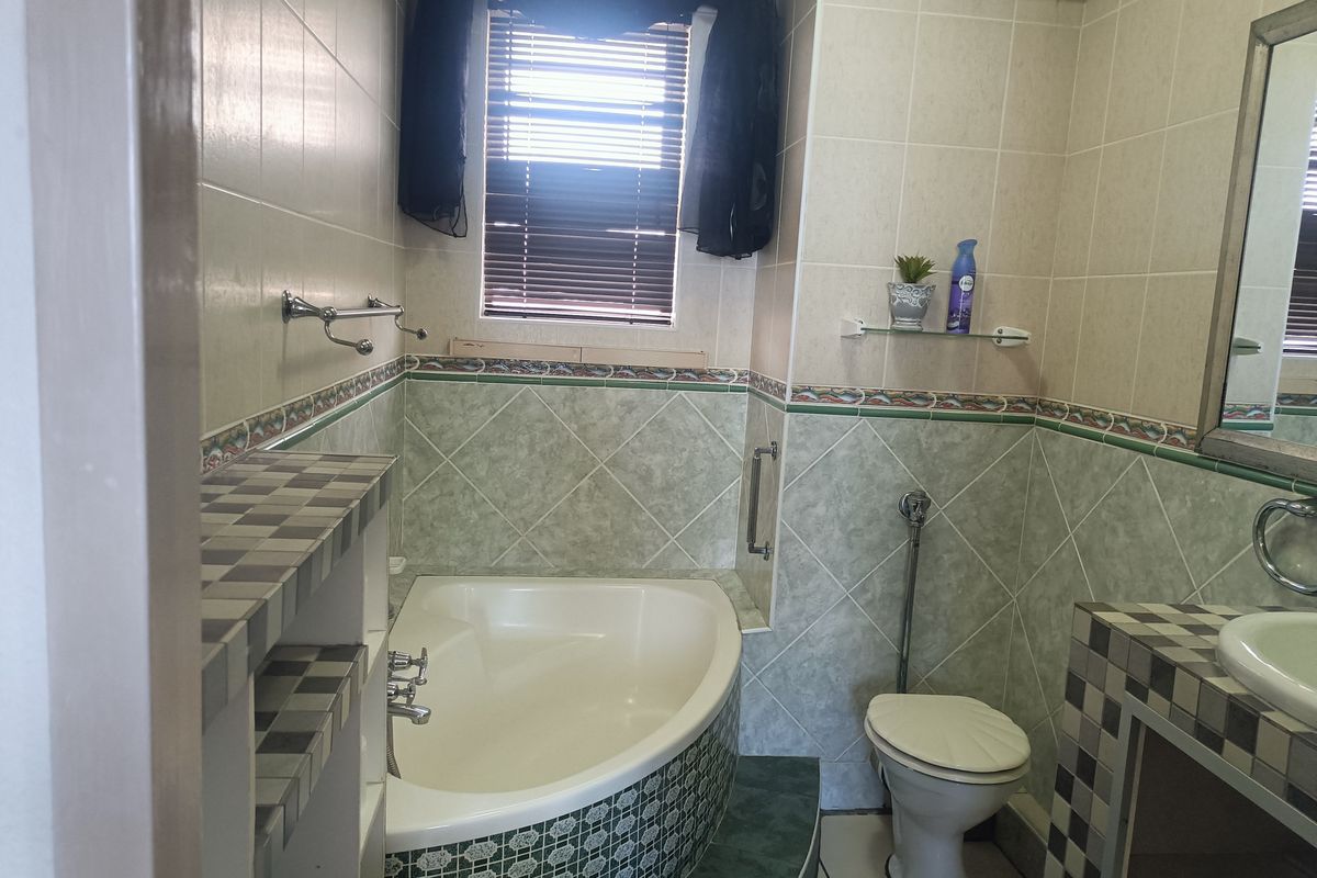 A bathroom featuring a corner bathtub, a built-in vanity with a basin, and tiled walls with decorative border accents.