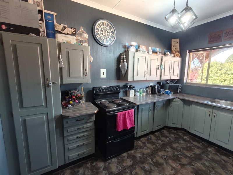 A functional kitchen featuring painted cabinetry, laminate countertops, a freestanding stove, and tiled flooring with natural light from a window with security bars.