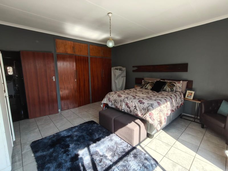 Spacious bedroom featuring tiled flooring, built-in wooden cupboards, and a fixed wooden headboard, offering a functional layout with ample storage space.