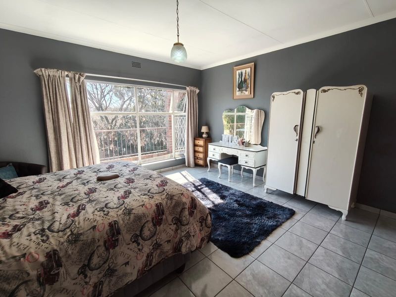 A spacious bedroom featuring large windows that provide ample natural light, tiled flooring, and a neutral wall finish.