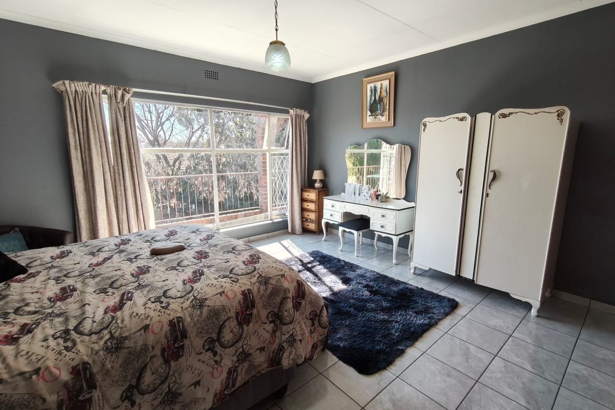 A spacious bedroom featuring large windows that provide ample natural light, tiled flooring, and a neutral wall finish.