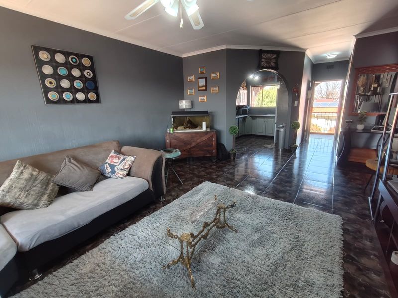 Open plan living area featuring dark tiled flooring, a decorative archway leading to the kitchen, and a ceiling fan.
