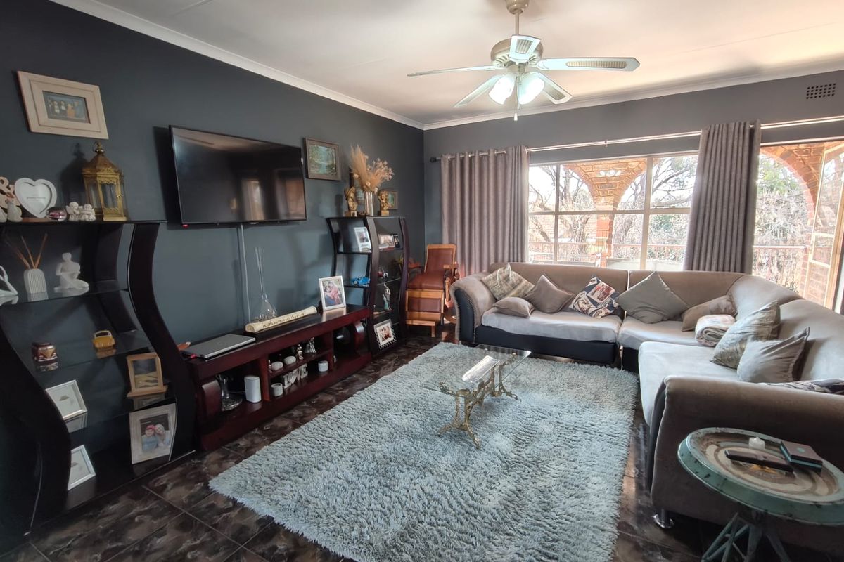 A comfortable living room featuring dark accent walls, tiled flooring, and a ceiling fan, with large windows providing natural light and outdoor views.