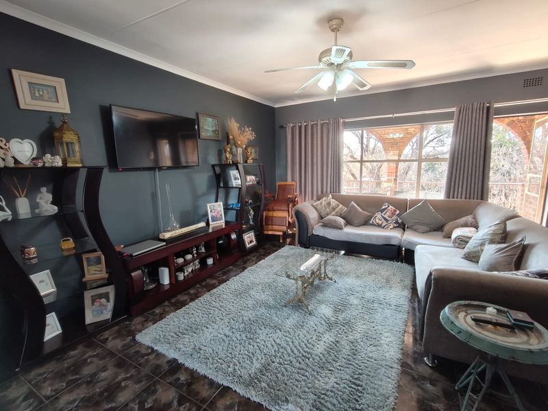 A comfortable living room featuring dark accent walls, tiled flooring, and a ceiling fan, with large windows providing natural light and outdoor views.