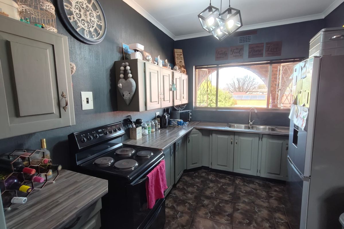 A functional kitchen featuring dark-toned walls, laminate countertops, built-in cabinetry, a double basin sink, and an electric stove with tiled flooring.
