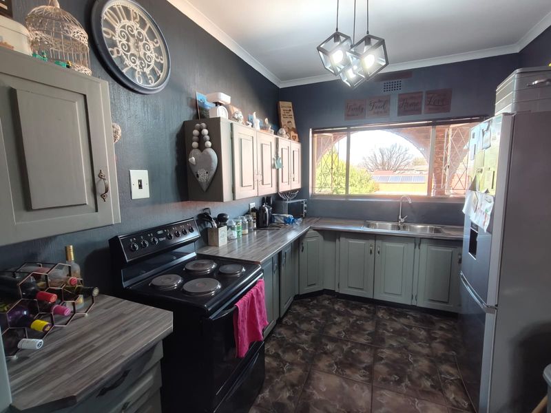 A functional kitchen featuring dark-toned walls, laminate countertops, built-in cabinetry, a double basin sink, and an electric stove with tiled flooring.