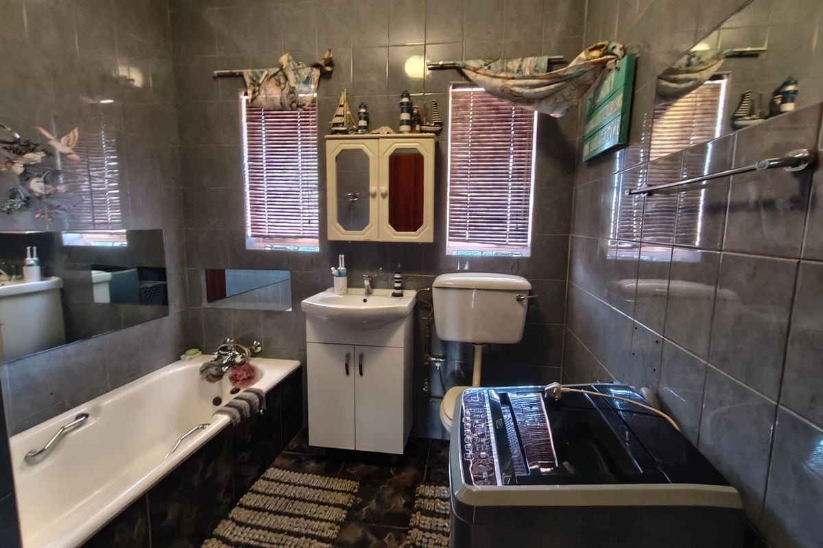 A functional bathroom featuring full-height wall tiling, a bathtub, a vanity basin, and a toilet, with integrated space for laundry appliances.