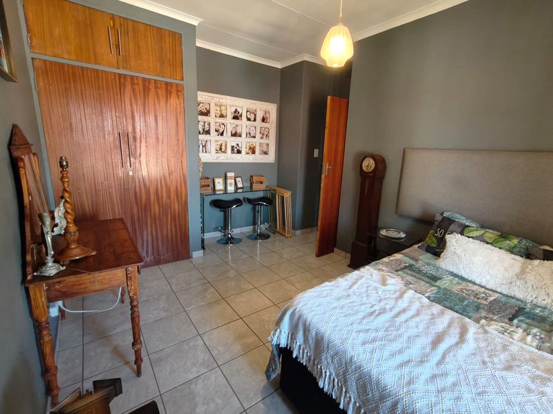 A bedroom featuring tiled flooring, coved ceilings, and built-in wooden cupboards, offering a functional space with neutral wall tones.