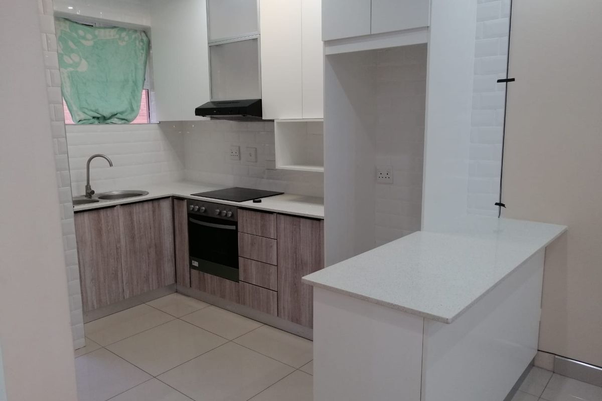 Modern kitchen featuring sleek white and wood-grain cabinetry, stone countertops, subway tile backsplash, and integrated appliances including an oven and hob.