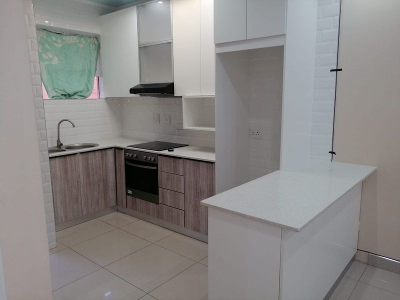 Modern kitchen featuring sleek white and wood-grain cabinetry, stone countertops, subway tile backsplash, and integrated appliances including an oven and hob.
