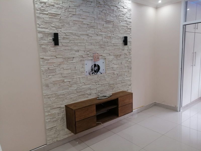 Living area featuring a textured stacked stone feature wall with integrated cabinetry and modern tiled flooring.
