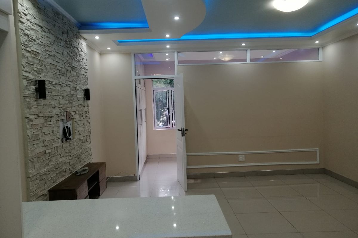 Spacious living area featuring a decorative stone accent wall, modern recessed ceiling with ambient LED lighting, and sleek tiled flooring throughout.