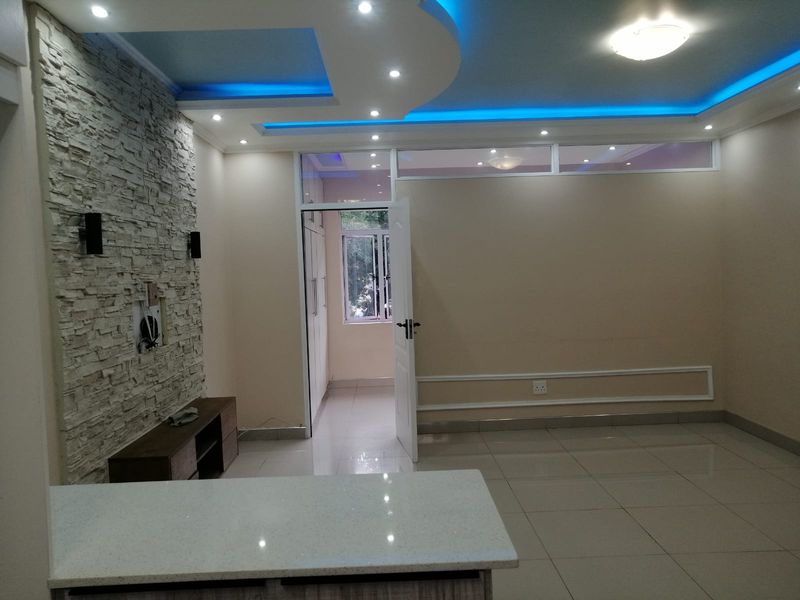 Spacious living area featuring a decorative stone accent wall, modern recessed ceiling with ambient LED lighting, and sleek tiled flooring throughout.