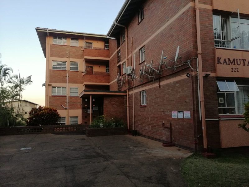 Exterior view of the brick apartment building facade featuring multiple balconies, security bars, and a paved driveway area.