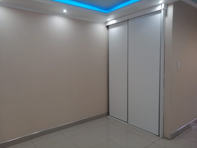 A clean, empty bedroom featuring modern tiled flooring, built-in sliding door wardrobes, and decorative recessed ceiling lighting with blue accent cove lighting.