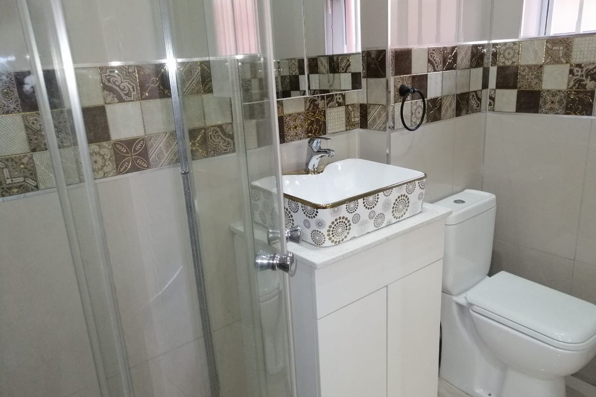 A modern bathroom featuring a glass shower enclosure, a decorative vessel sink with vanity cabinet, and stylish patterned wall tiling.