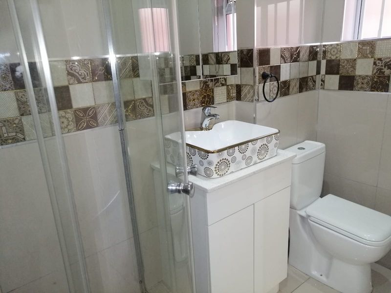 A modern bathroom featuring a glass shower enclosure, a decorative vessel sink with vanity cabinet, and stylish patterned wall tiling.