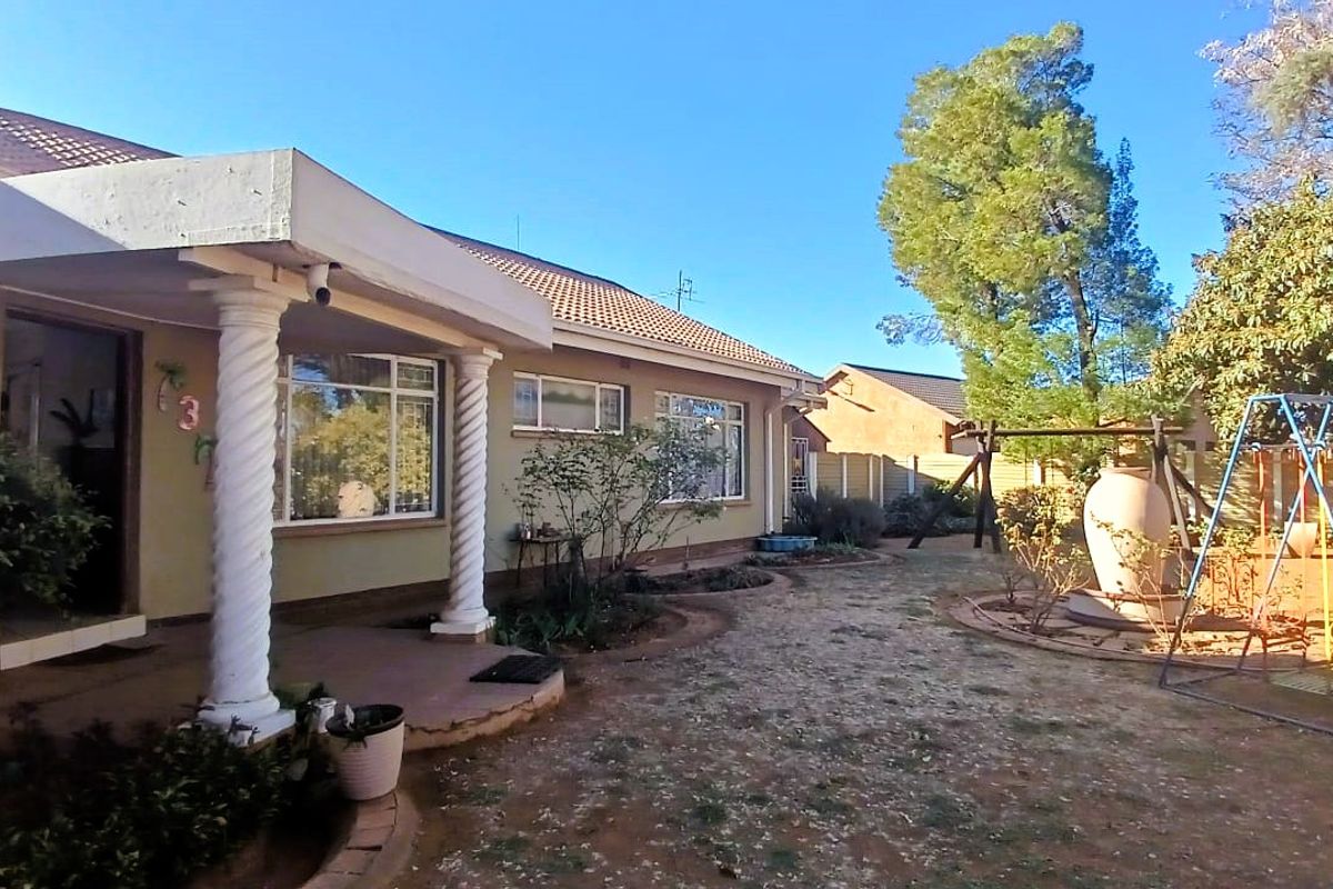 Rear view of the house featuring a covered patio with decorative columns, overlooking a garden area with established landscaping and paved sections.