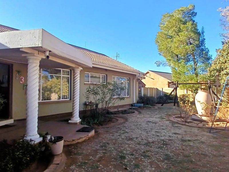 Rear view of the house featuring a covered patio with decorative columns, overlooking a garden area with established landscaping and paved sections.