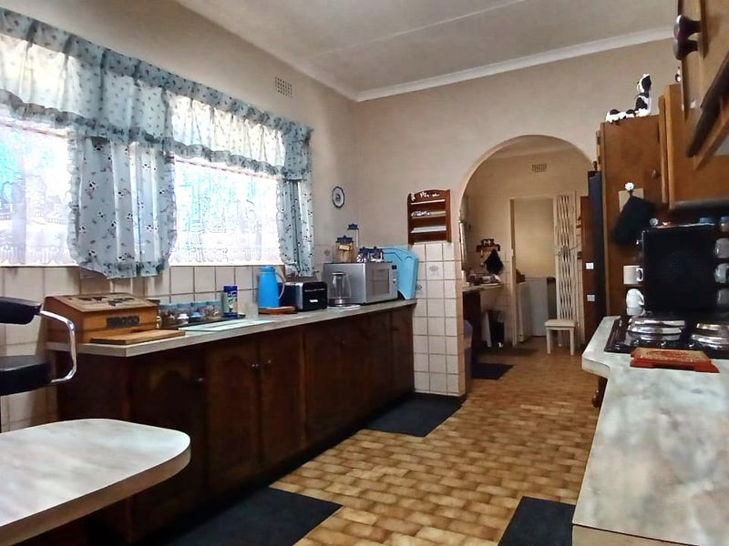 A dated kitchen featuring traditional wooden cabinetry, laminate countertops, a gas hob, and an arched doorway leading to an adjacent utility area.