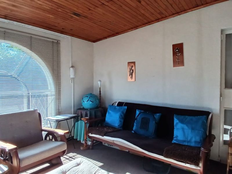 A living room featuring a distinctive timber-clad ceiling and a large arched window with venetian blinds, offering a dated but functional living space.