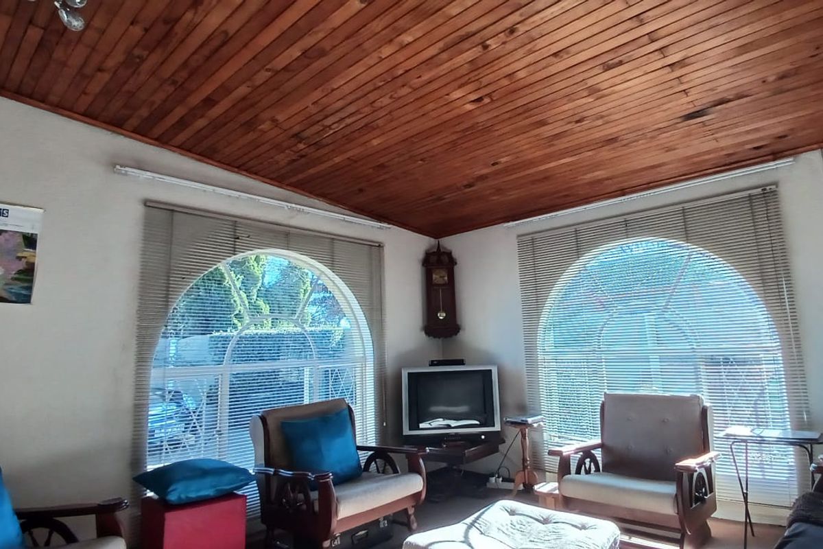 A living room featuring a warm timber-clad ceiling and distinctive arched windows with venetian blinds, offering a cozy and traditional atmosphere.