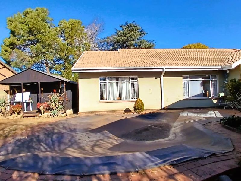 Rear view of the property featuring a paved patio area, a swimming pool with a cover, and a detached timber gazebo in the garden.