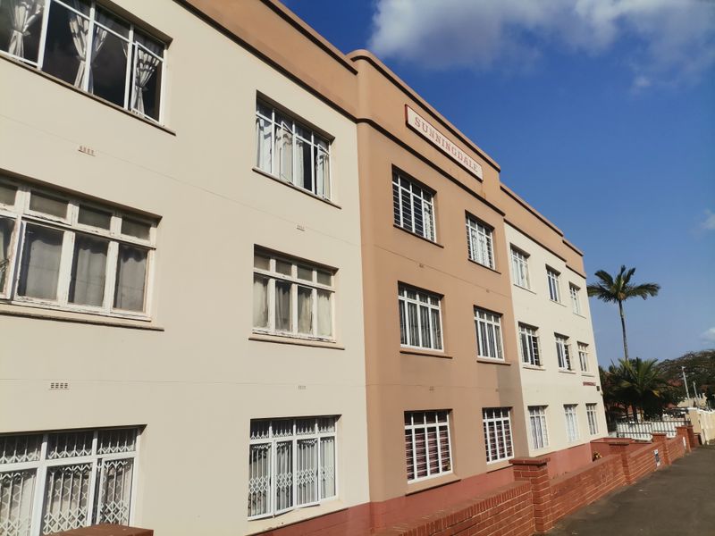 A view of the Sunningdale apartment building facade, featuring multi-story architecture with casement windows and a brick boundary wall.