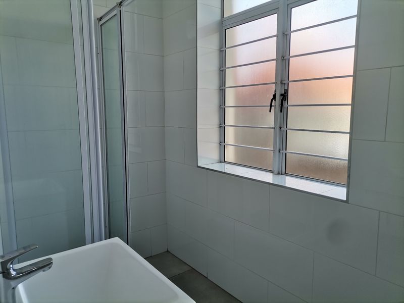 A clean, modern bathroom featuring a glass shower enclosure, a white basin with a mixer tap, and tiled walls with a frosted window.