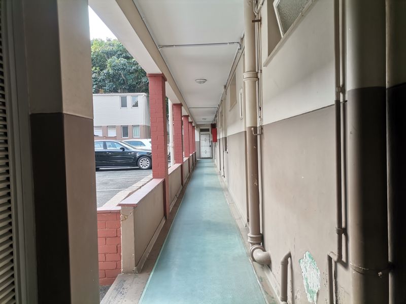 An exterior covered walkway or corridor featuring brick pillars and painted concrete flooring, providing access to the apartment units.
