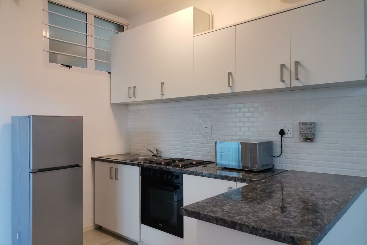 A clean, functional kitchen featuring white cabinetry, dark laminate countertops, a subway tile backsplash, and integrated oven and hob.