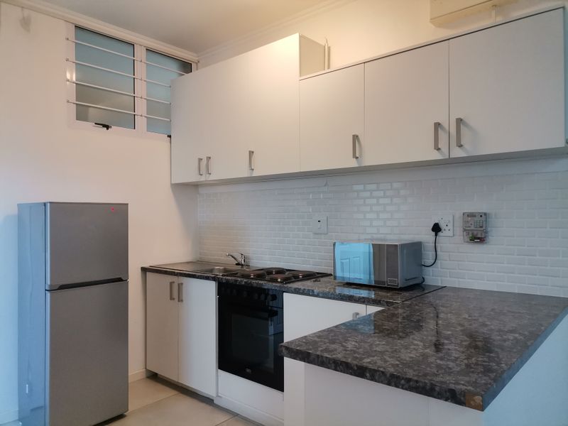A clean, functional kitchen featuring white cabinetry, dark laminate countertops, a subway tile backsplash, and integrated oven and hob.