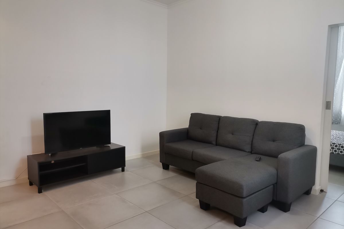 A simple living room featuring neutral tiled flooring and plain white walls, offering a clean and functional space.