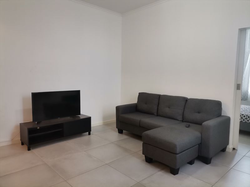 A simple living room featuring neutral tiled flooring and plain white walls, offering a clean and functional space.